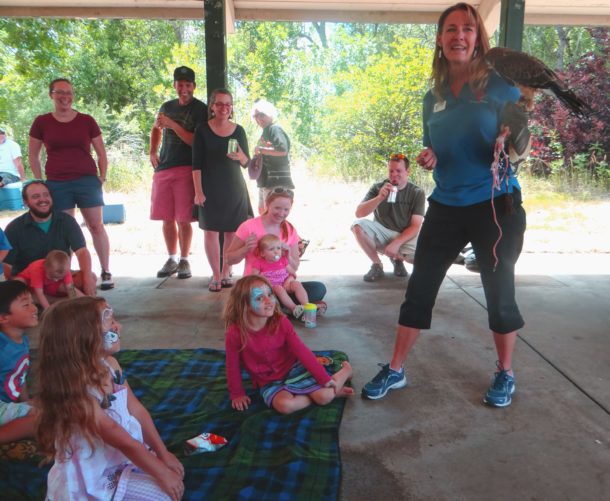 woman holding bird on arm with kids sitting on the ground watching