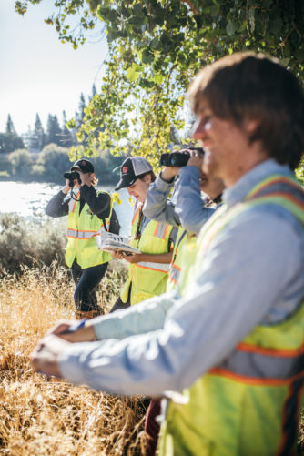 GEI employees in yellow vests looking through binoculars