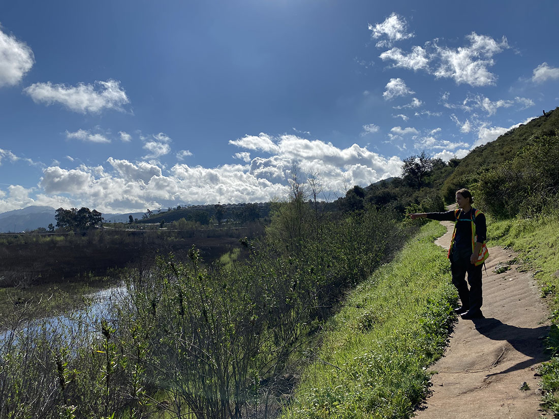 Woman walking along bank of waterbody, pointing to water