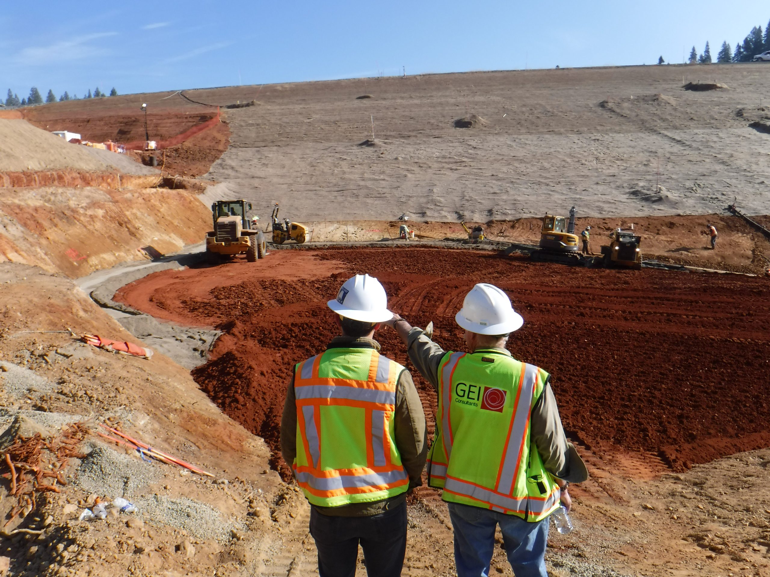 Men in construction helmets and safety vest standing in front of the El Dorado Forebay Dam construction.
