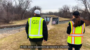 Man and woman in safety vests walking alongside a levee.