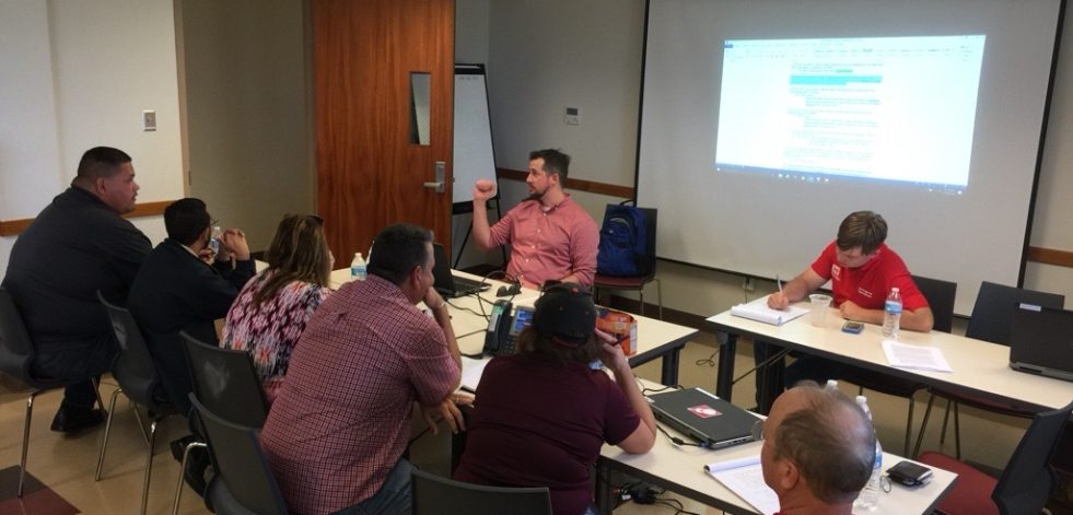 Man teaching in classroom with men and women at tables listening