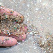 Close-up side shot of hands shows microplastic waste contaminated with the seaside sand.